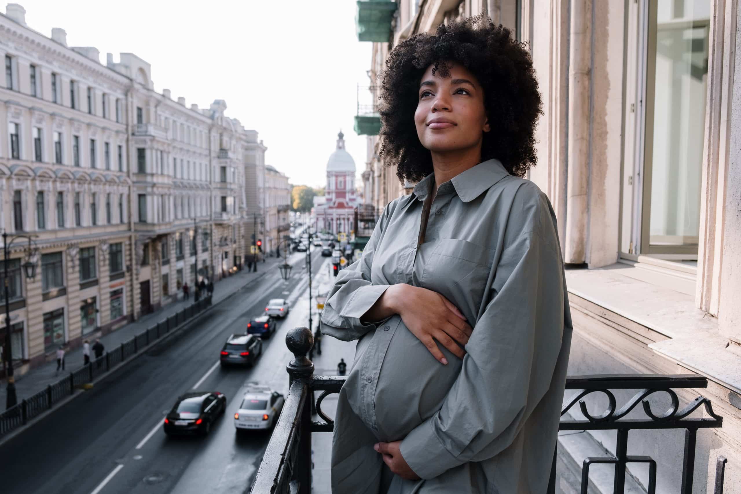 zwangere vrouw lacht op balkon met handen op haar buik